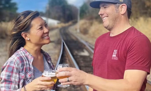 man and woman holding beers by a railroad